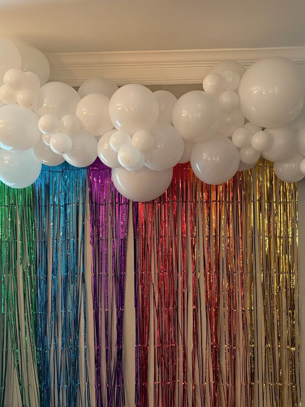 White balloon garland above a rainbow fringe curtain backdrop
