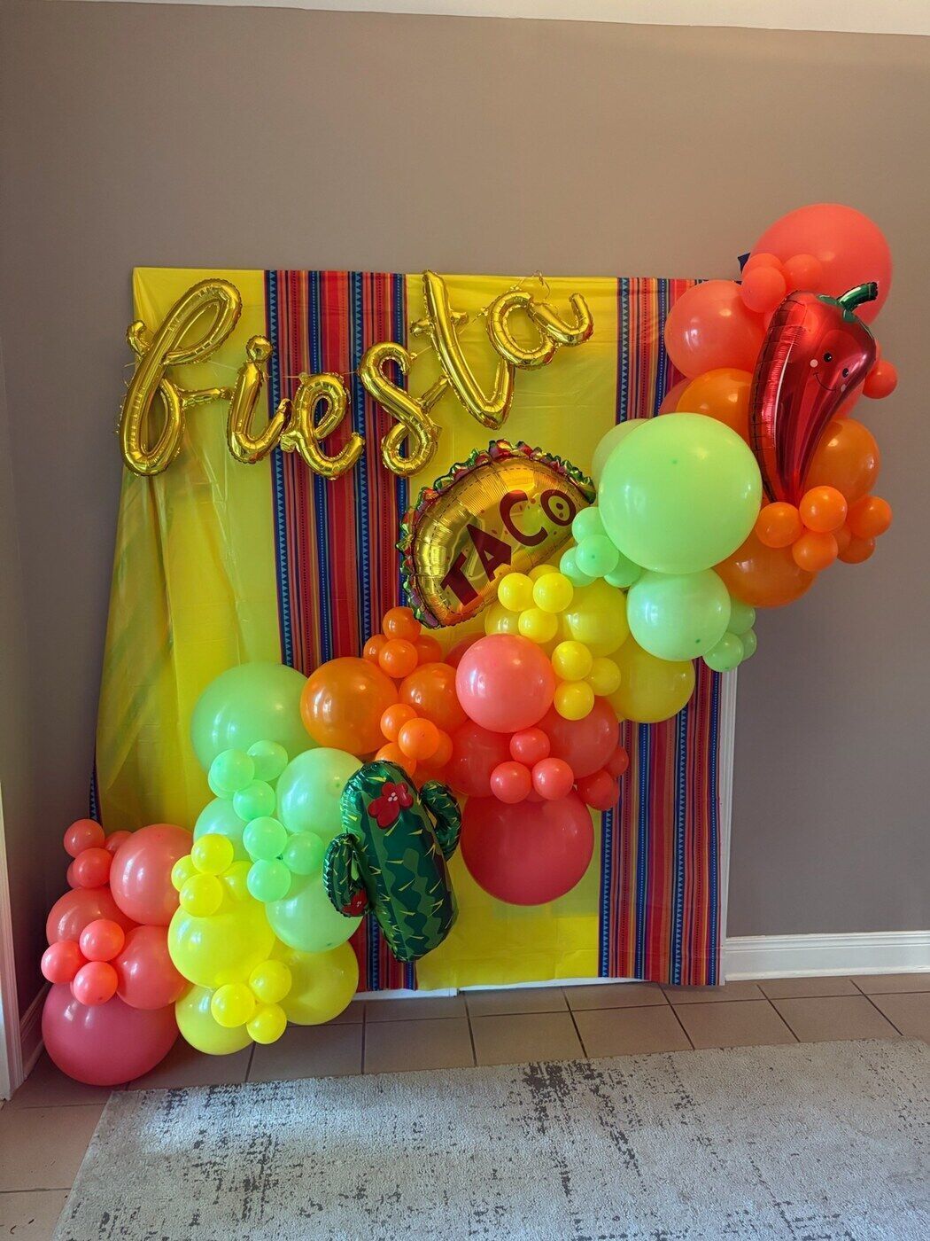 Fiesta themed balloon arch in red, green and yellow with a serape backdrop