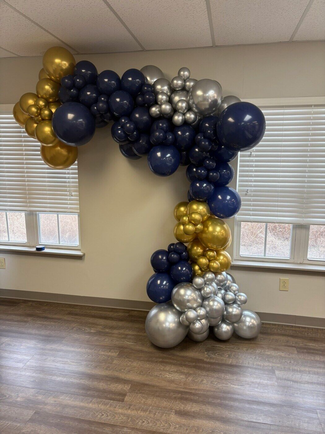 Navy, gold and silver balloon arch across a bright window wall