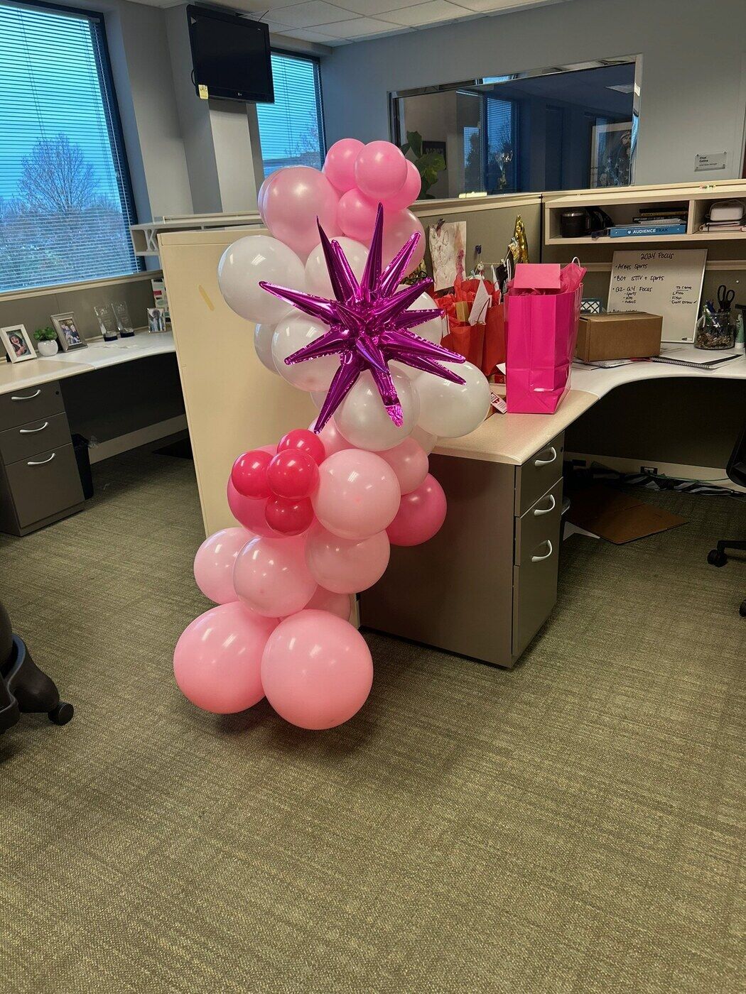 Pink balloon garland and a purple starburst on an office desk