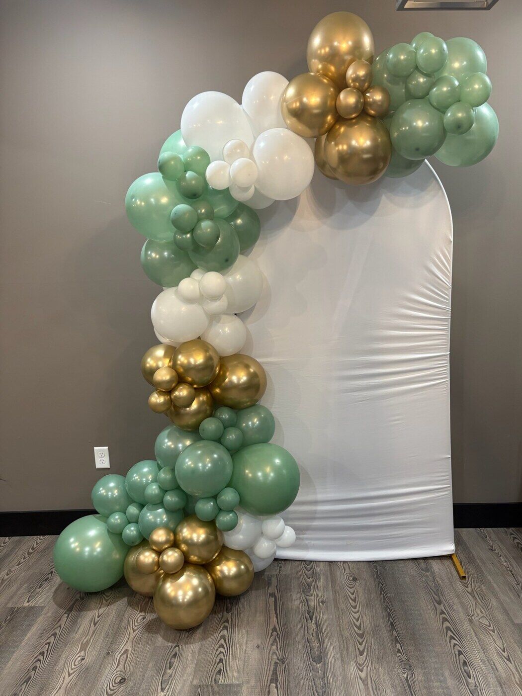 Sage green and gold balloon garland on a white arch backdrop